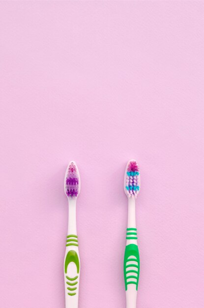 Dos cepillos de dientes se encuentran sobre un fondo rosa pastel