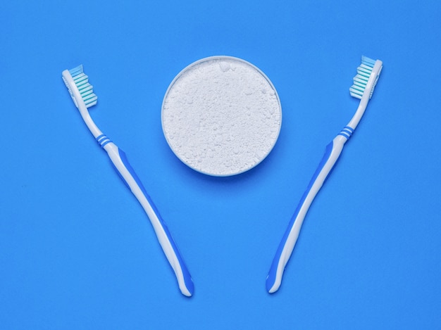 Foto dos cepillos de dientes y un frasco de polvo de dientes sobre la mesa azul. la vista desde la cima. endecha plana.