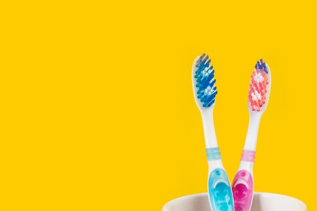 Dos cepillos de dientes de plástico de color en un vaso de cerámica sobre un fondo amarillo