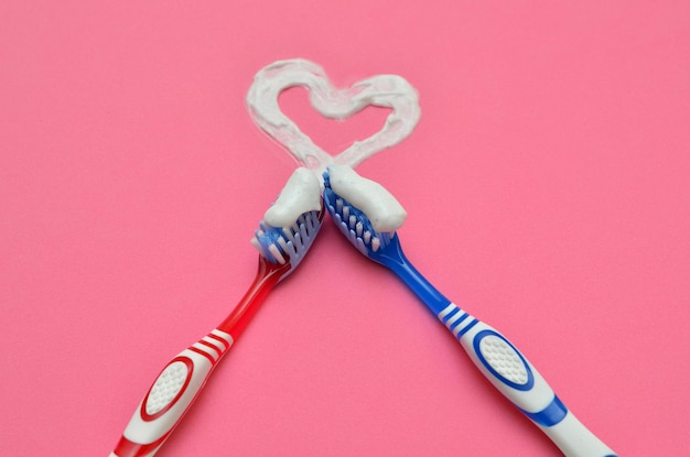 Dos cepillos de dientes y un símbolo de amor del corazón de pasta de dientes en un fondo rosa