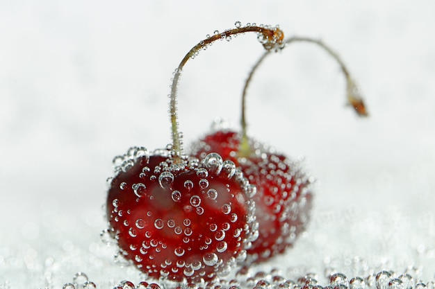 Dos cerezas dulces en burbujas de gas en un rosa claro borrosa