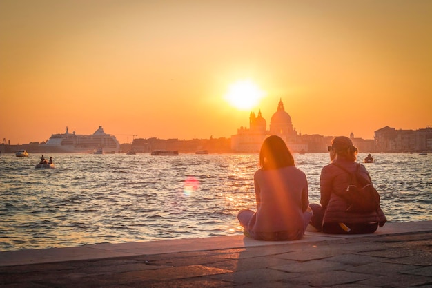 Dos chicas admiran la pintoresca puesta de sol sobre Santa Maria della Salute en Venecia.