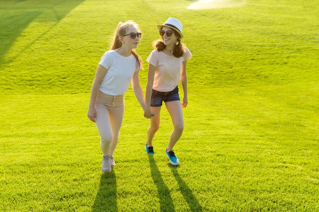 Dos chicas adolescentes se dan la mano sobre la hierba verde en el parque en un caluroso día de verano