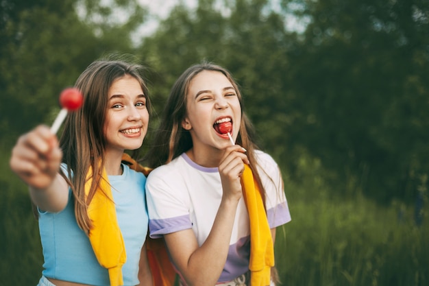 Dos chicas adolescentes divertidas sosteniendo un caramelo de lollipop rojo brillante