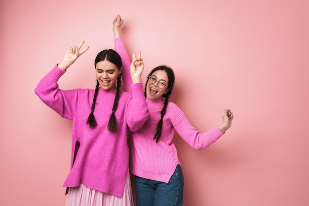 Dos chicas adolescentes lindas alegres bailando aislado sobre pared rosa, divirtiéndose