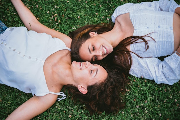 Dos chicas adolescentes sonriendo y mirándose mientras están tumbadas en el césped en un parque