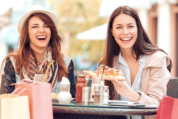 Dos chicas alegres comiendo pizza en un café al aire libre