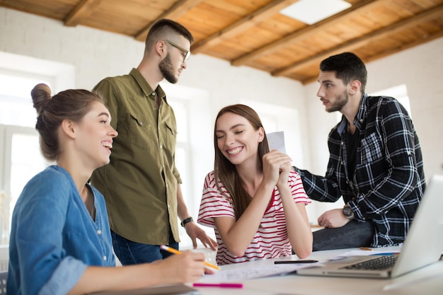 Dos chicas alegres se ríen felizmente mientras pasan tiempo en la oficina moderna con colegas en el fondo Grupo de personas creativas trabajando juntas