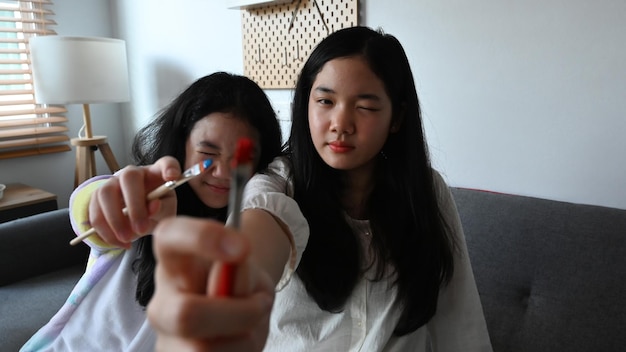 Dos chicas asiáticas juguetonas sosteniendo pinceles y sonriendo a la cámara