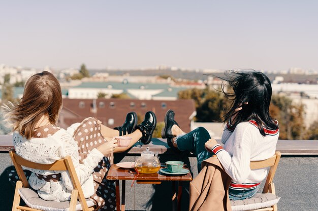 Dos chicas atractivas disfrutan de una fiesta de té en la azotea con vistas a la ciudad