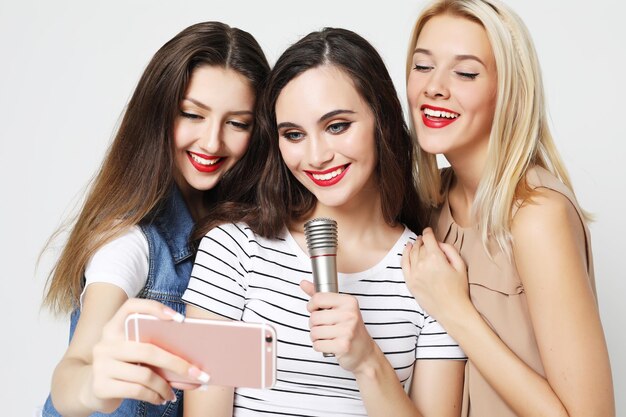 Dos chicas de belleza con un micrófono toman selfie con teléfono inteligente