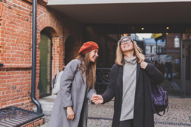 Dos chicas caminando juntas en la calle y tomándose de la mano Visten ropa de primavera u otoño y son felices Concepto de amistad y relación