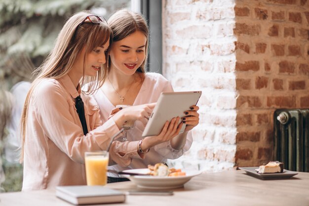 Dos chicas de compras en tableta en un café