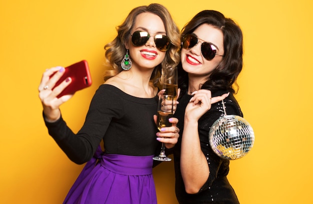 Dos chicas con copa de vino y bolas de discoteca hacen selfie feliz y sonríen