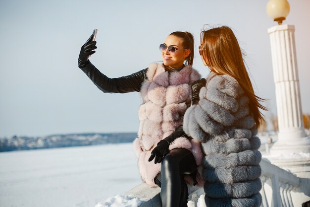 dos chicas elegantes y magníficas con elegantes abrigos de pieles caminando en el parque de invierno