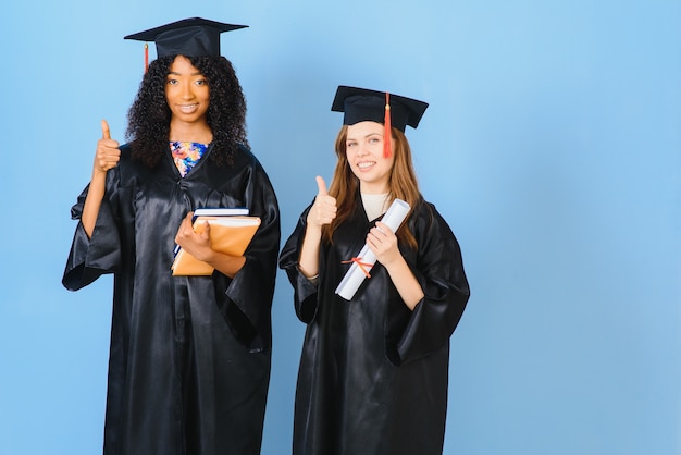 Dos chicas están posando para tomar una foto en vestidos negros y tienen certificado de diploma. Son graduados y poseen certificado de diploma. Están felices y de buen humor.