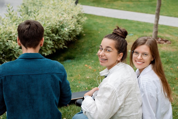 Dos chicas estudiantes con gafas sonriendo miran a la cámara el chico está trabajando en la computadora