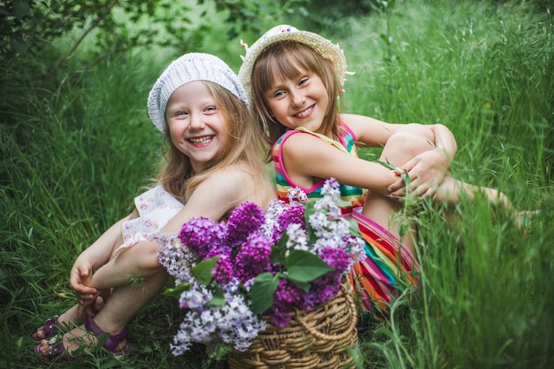 Dos chicas europeas riendo con gorras blancas se sientan en un jardín de verano en el suelo con una cesta de colo