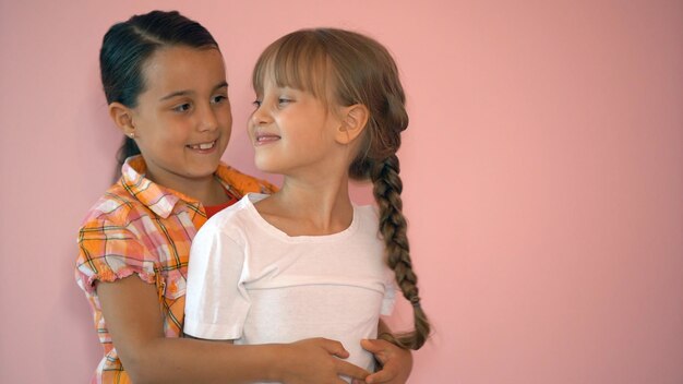 Foto dos chicas felices abrazándose unas a otras aisladas de fondo rosa