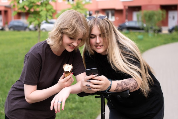 Dos chicas graciosas están sentadas en un columpio en la ciudad y tomando selfies en su teléfono.