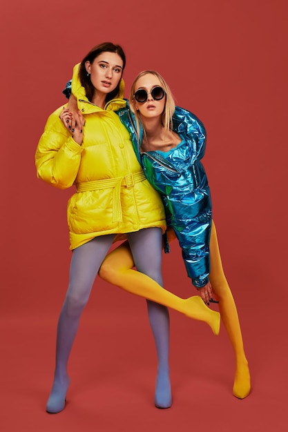 Dos chicas guapas en bocanadas posando para la cámara en el estudio. Rubia y morena con medias lucen seguras frente a la cámara, abrazándose