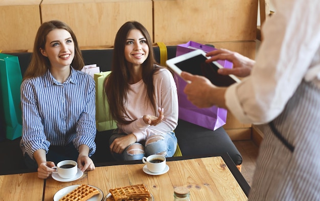 Dos chicas guapas coqueteando con el camarero en el café, tableta digital con pantalla en blanco negra