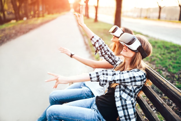 Dos chicas guapas disfrutan de gafas de realidad virtual al aire libre.