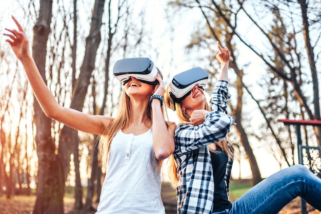 Dos chicas guapas disfrutan de gafas de realidad virtual al aire libre.