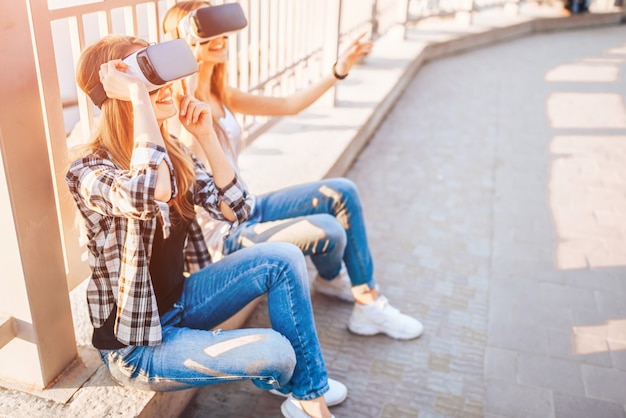 Dos chicas guapas disfrutan de gafas de realidad virtual al aire libre.