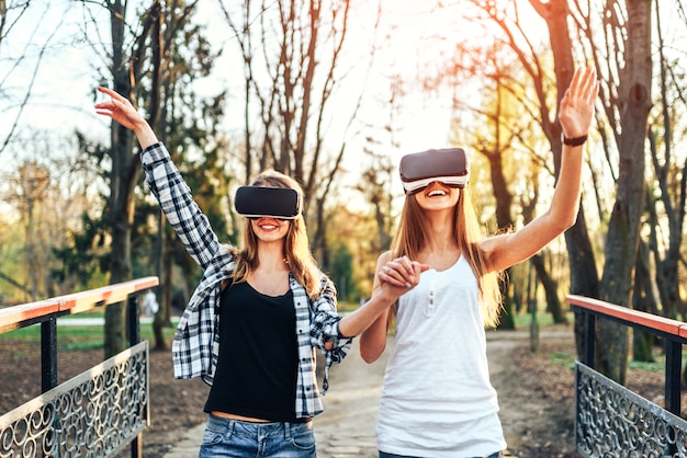 Dos chicas guapas disfrutan de gafas de realidad virtual al aire libre.