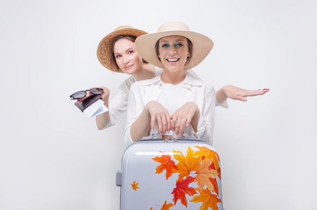 Dos chicas guapas posando sobre un fondo blanco antes de ir de viaje. Concepto de turismo.