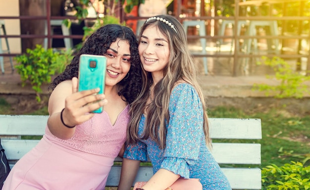 Dos chicas guapas sentadas en un banco tomando un selfie chicas sonriendo y tomando un concepto de amistad entre hermanas selfie