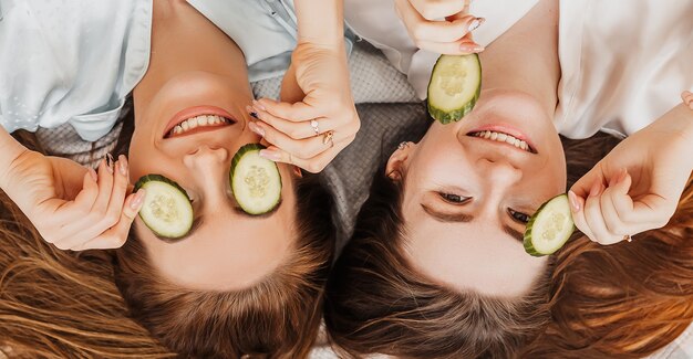 Dos chicas hacen máscaras de belleza caseras para el rostro y el cabello. Pepinos para la frescura de la piel del contorno de ojos.