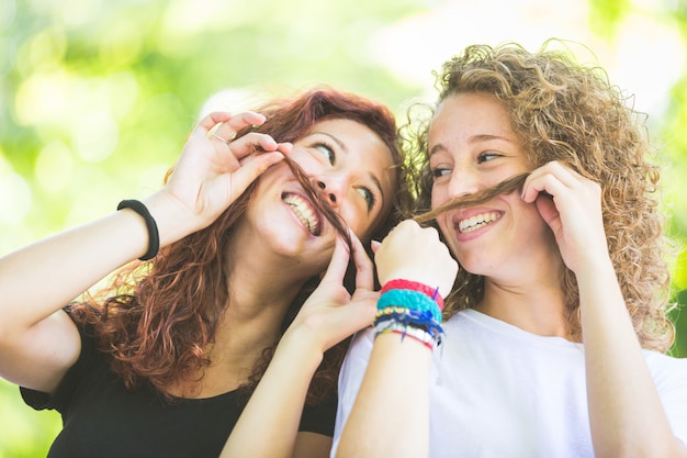 Dos chicas haciendo bigote con el pelo.