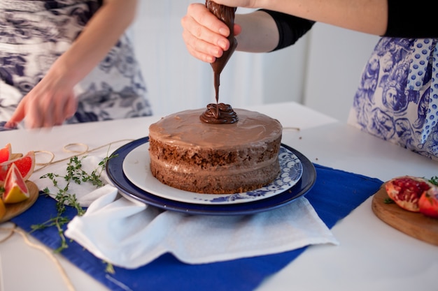 Dos chicas haciendo un pastel en la cocina. Mano femenina exprime la crema de chocolate