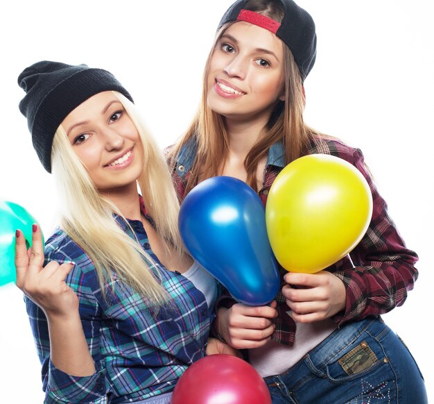 Dos chicas hipster felices sonriendo y sosteniendo globos de colores sobre fondo blanco.