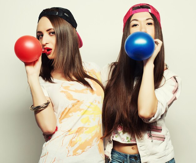 Dos chicas hipster felices sonriendo y sosteniendo globos de colores sobre fondo blanco.