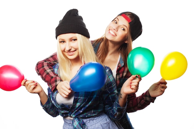 Dos chicas hipster felices sonriendo y sosteniendo globos de colores sobre fondo blanco.