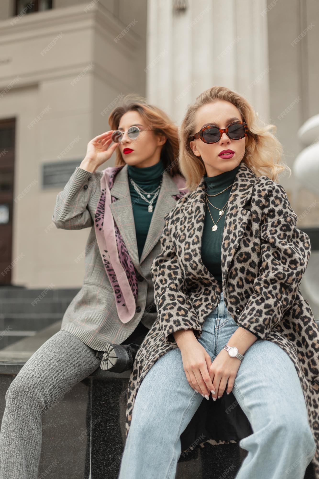 Dos chicas hipster de moda usan de sol de moda en elegantes azules con abrigo de leopardo y sientan y posan en la ciudad ropa de estilo femenino