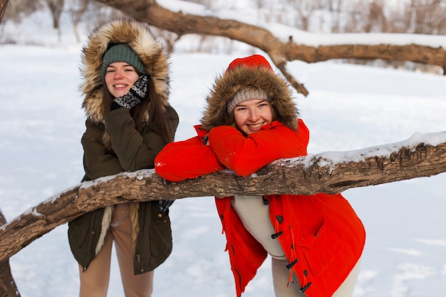 Dos chicas en invierno, en ropa de abrigo, disfrutando de la nieve, al aire libre. Época fría del año, risas y diversión. Bosque de invierno, claro blanco.