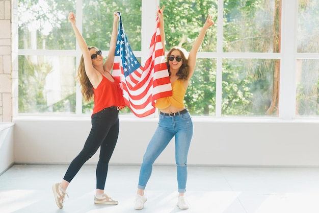 Dos chicas jóvenes atractivas con gafas de sol con la bandera estadounidense Celebraciones del día de la independencia de Estados Unidos