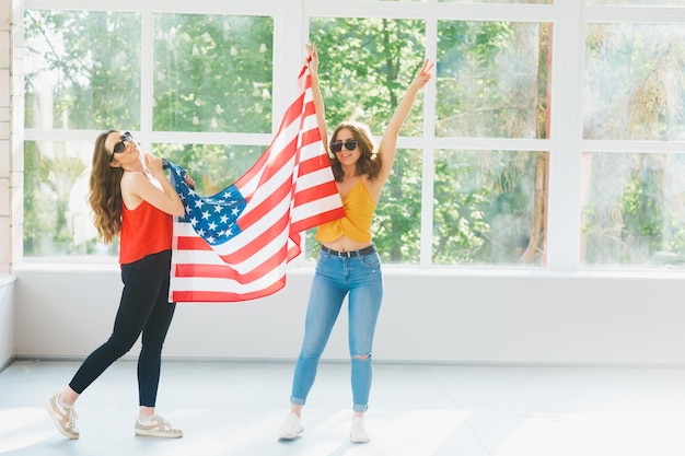 Dos chicas jóvenes atractivas con gafas de sol con la bandera estadounidense Celebraciones del día de la independencia de Estados Unidos