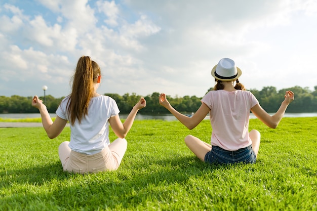 Dos chicas jóvenes haciendo yoga plantean al aire libre