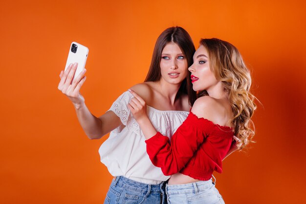 Dos chicas jóvenes y hermosas se toman una selfie y miran el teléfono en un espacio morado. Chicas para publicidad.