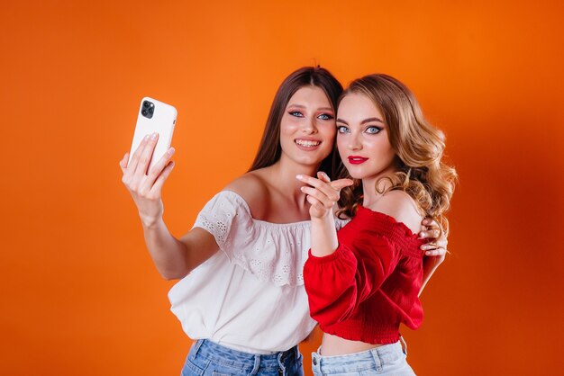 Foto dos chicas jóvenes y hermosas se toman un selfie y miran el teléfono en el estudio sobre un fondo morado. chicas para publicidad.