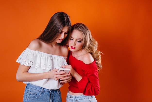 Dos chicas jóvenes y hermosas se toman un selfie y miran el teléfono en una pared violeta. Chicas para publicidad.