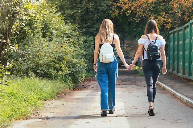 Dos chicas jóvenes con mochilas cogidas de la mano de espaldas a nosotros foto de alta calidad