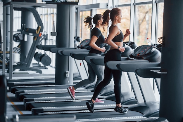 Dos chicas jóvenes en ropa deportiva están juntas en el gimnasio en la caminadora.