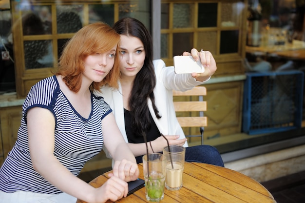 Dos chicas jóvenes tomando un autorretrato (selfie) con teléfono inteligente