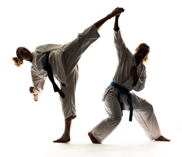 Dos chicas en kimonos blancos con cinturones negros y azules, entrenando y practicando stands y técnicas de karate